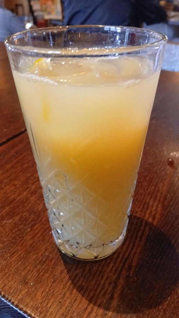 A close up of an orange and yellow drink in a glass with ice cubes.